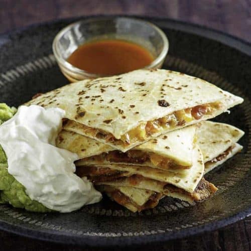 Cheese and bacon quesadilla cut into pieces served with sour cream, guacamole, and sour cream.