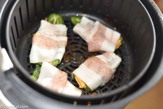 Bacon wrapped jalapeno poppers inside of an air fryer.