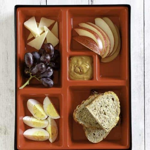 Slices of eggs, cheese, apples, and bread in a red bento box.