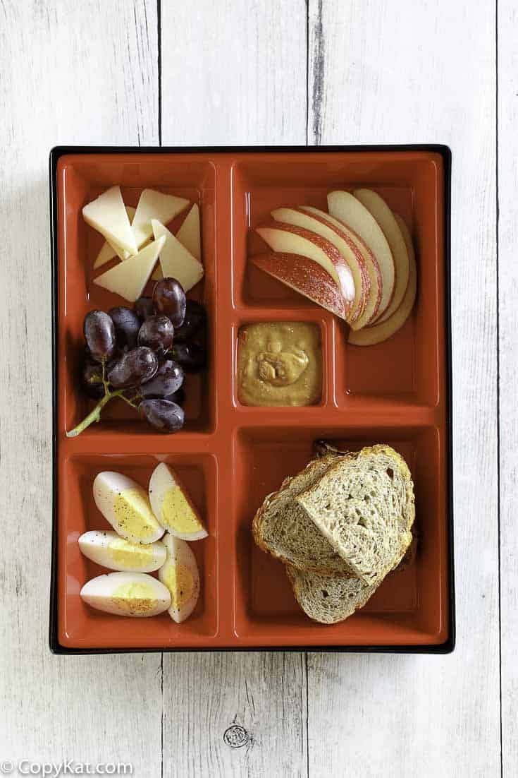 Slices of eggs, cheese, apples, and bread in a red bento box.