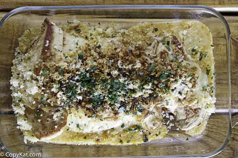 An overhead shot of a glass baking dish containing the finished parmesan crusted chicken. The chicken is covered in a creamy sauce and a toasted panko breadcrumb topping garnished with herbs.