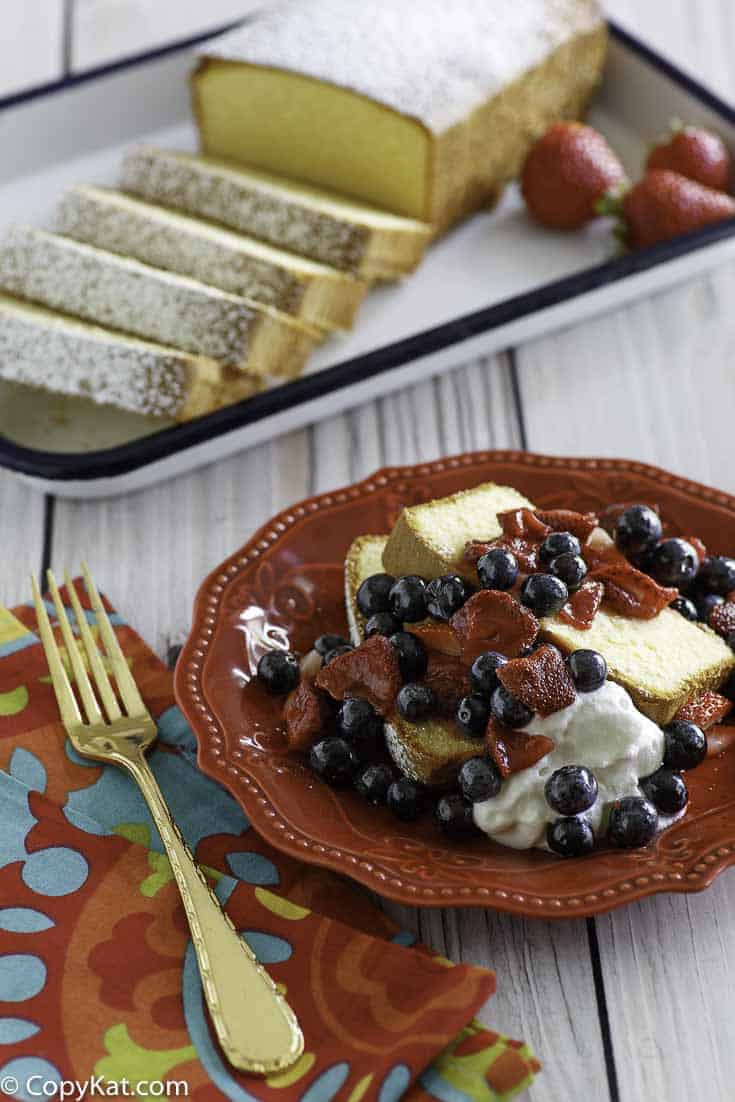 Homemade copycat Sara Lee Pound Cake and fruit on a plate in front of the cake on a serving platter.