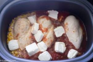 Adding cream cheese to the crockpot of chicken and black beans and corn