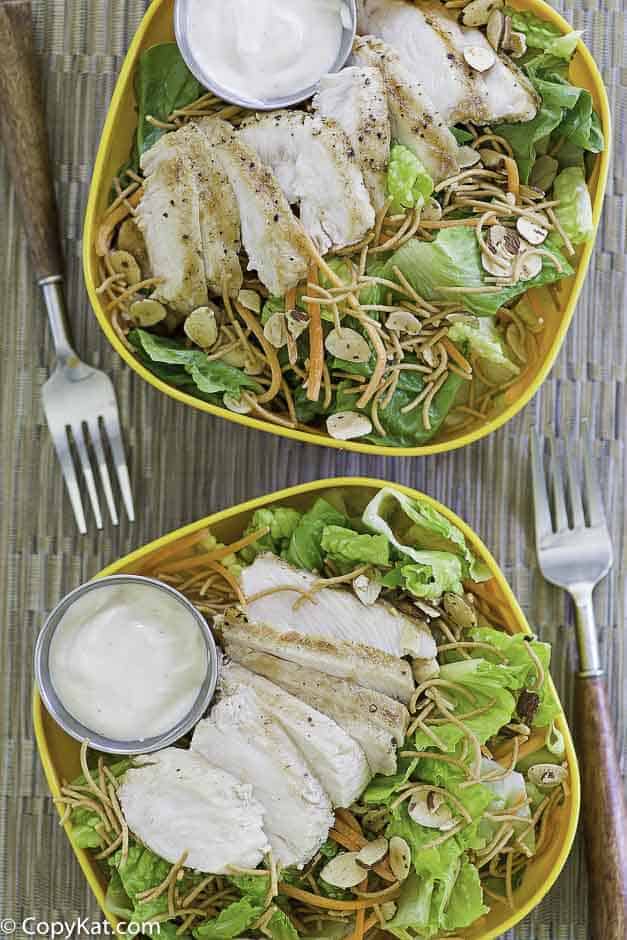 Two bowls of salad with grilled chicken and oriental dressing