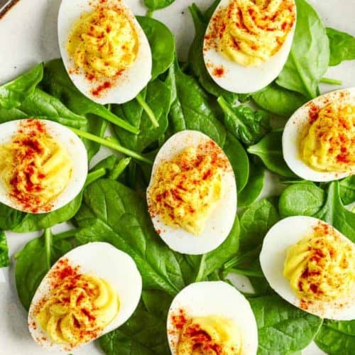 a plate of deviled eggs on top of fresh spinach leaves