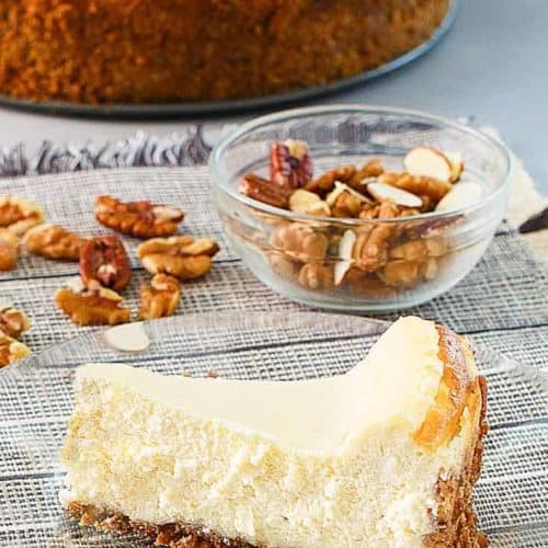 a slice of cheesecake, nuts, and a cheesecake on platter