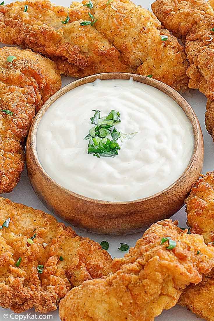 a bowl of Jan sauce with chicken tenders around it