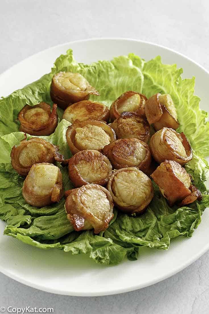 bacon wrapped scallops on top of lettuce on a platter