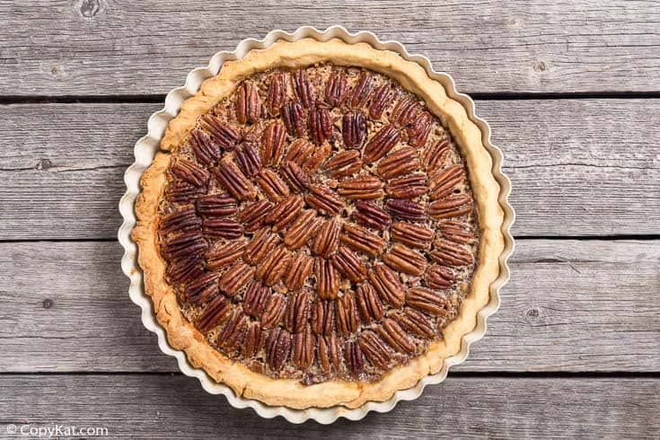 An overhead, flat-lay view of a whole, freshly baked Luby's pecan pie in a fluted pan. The pecan halves are arranged in a decorative circular pattern on top of the rich filling.