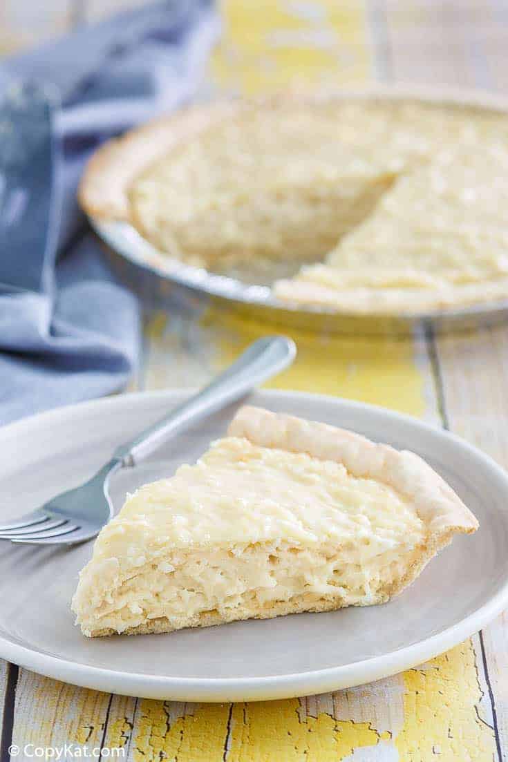 coconut cream pie slice on a plate with the pie on the table behind it