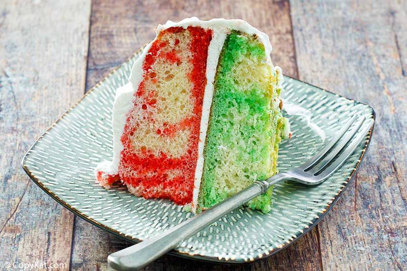 Close up of a slice of layered cake showing red and green Jello streaks inside.