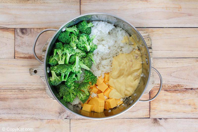 An overhead view looking into a large saucepan filled with the ingredients for broccoli cheese rice casserole. The unmixed components—broccoli florets, cooked rice, cubed Velveeta cheese, and cream of chicken soup—are shown ready to be combined.