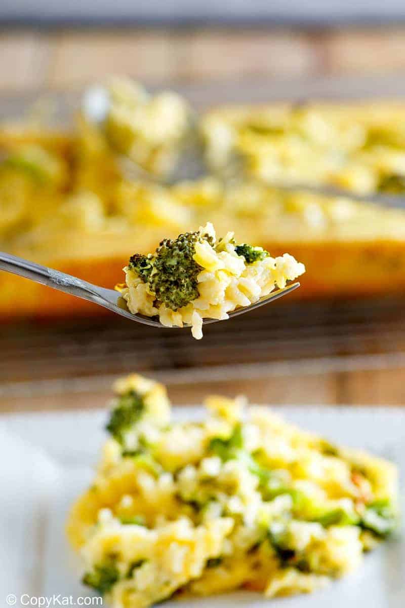 A macro shot focusing on a fork lifting a perfect bite of broccoli cheese rice casserole. The bite highlights the creamy rice and a tender piece of broccoli, with the rest of the plated serving blurred in the background.