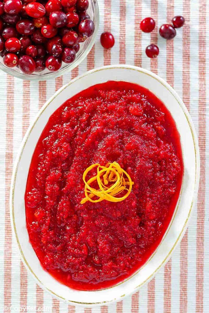 An overhead, flat-lay view of a serving dish of fresh Luby's cranberry relish. The vibrant red relish is garnished with orange zest, with a bowl of whole cranberries nearby.