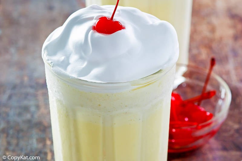 A close-up of a McDonald's eggnog shake topped with a mound of whipped cream and a bright red maraschino cherry.