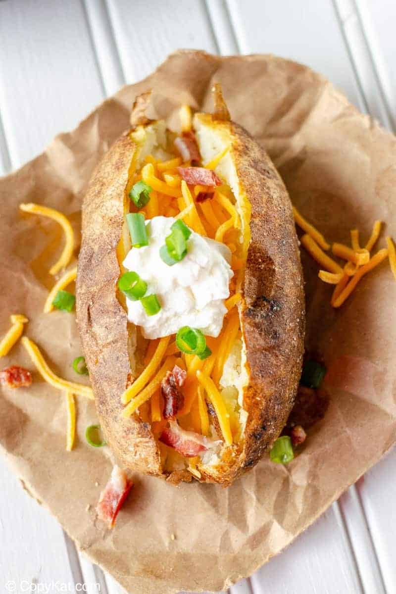 air fryer baked potato topped with butter, cheese, sour cream, bacon, and chives