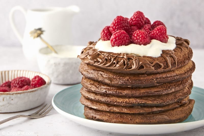 a stack of six chocolate pancakes, raspberries, cream, and a small pitcher
