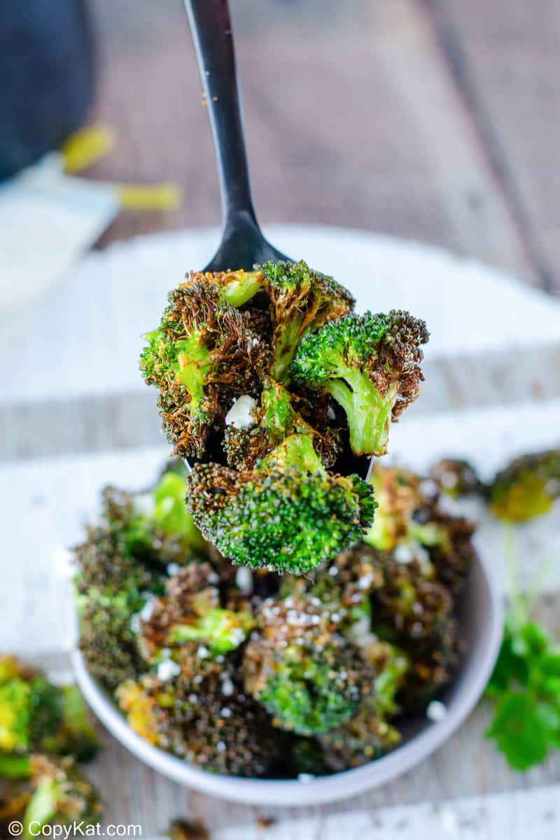 air fryer broccoli on a spoon over a bowl of air fried broccoli
