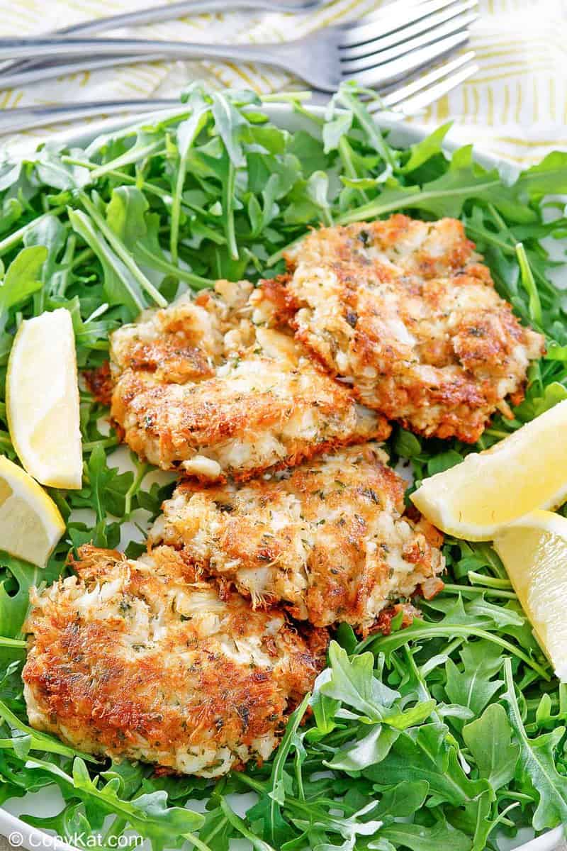 four Maryland crab cakes, lemon wedges, and arugula on a platter