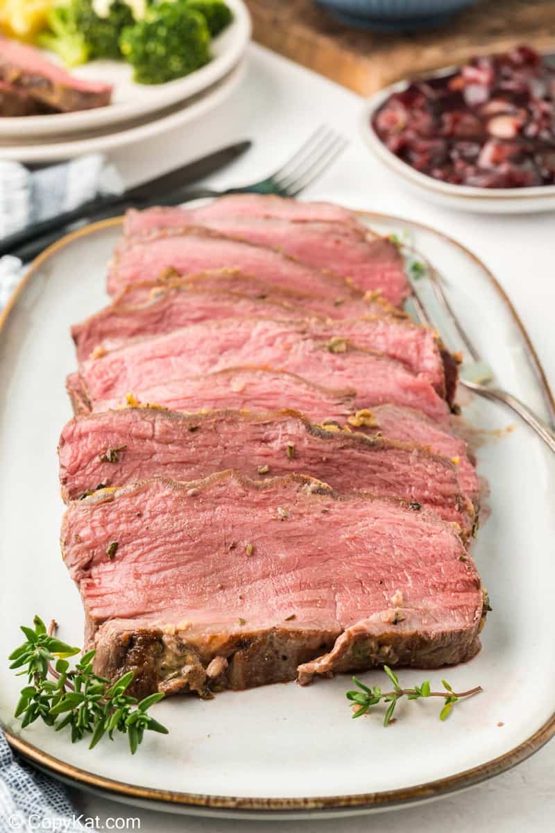 Several thick, juicy slices of New York Strip roast, cooked to a perfect medium-rare, are elegantly arranged on a serving platter and garnished with fresh thyme.