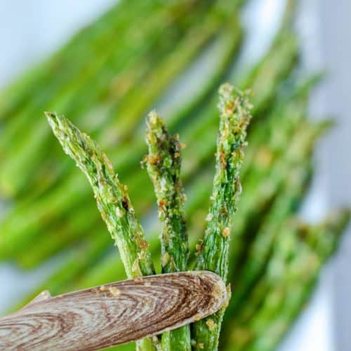 three air fried asparagus spears held by tongs