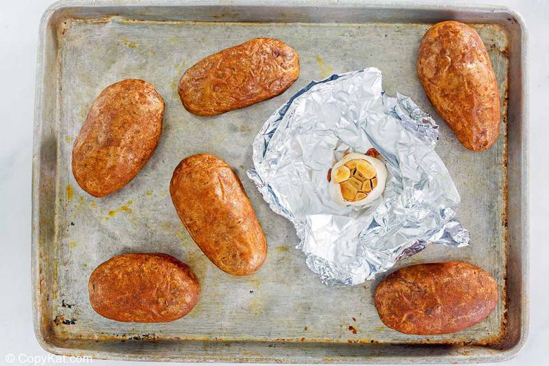 baked potatoes and roasted garlic bulb on a baking sheet