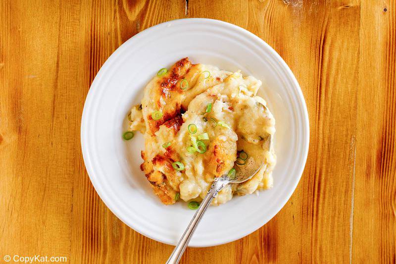 baked potato casserole topped with green onions on a white plate.