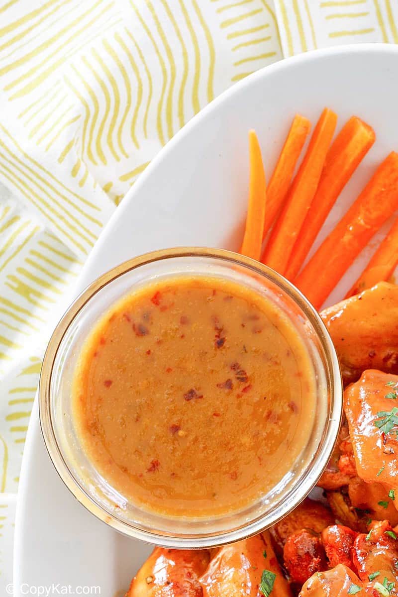 a bowl of mustard bbq sauce, carrot sticks, and wings on a platter
