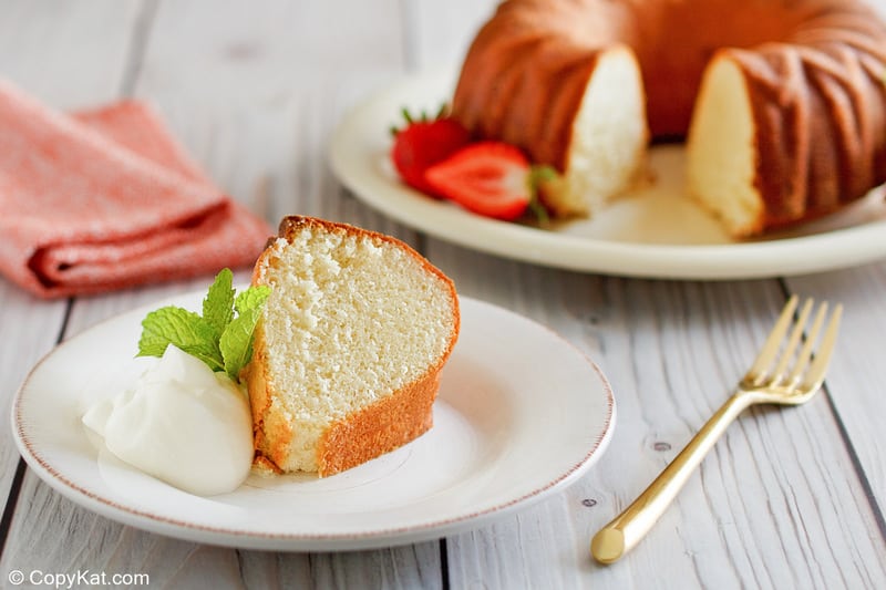 A slice of Scandinavian almond cake on a white plate, served with whipped cream, mint, and a gold fork.