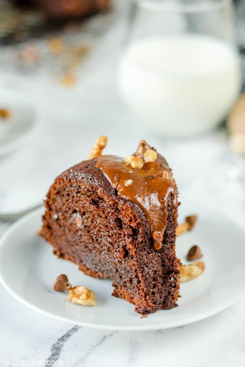 A close-up of a single slice of moist chocolate bundt cake, topped with a thick caramel glaze, walnuts, and chocolate chips.