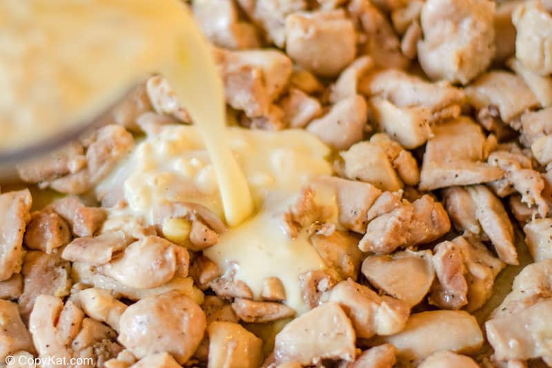 pouring a casserole mixture over cooked chicken pieces.