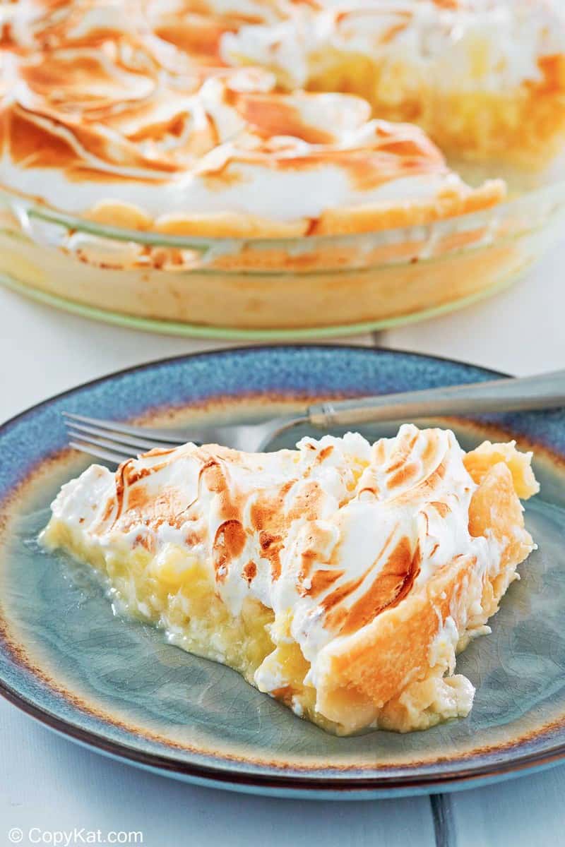 a slice of lemon meringue pie on a plate with the pie behind it