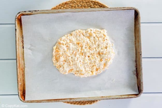 Raw cheddar biscuit dough patted into a rough circle on a parchment-lined baking sheet.