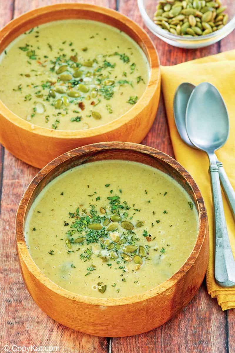 two bowls of acorn squash soup, a bowl of pumpkin seeds, and two spoons.