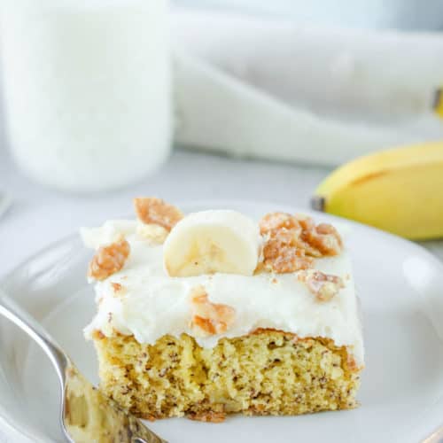 banana cake slice and a fork on a plate and a glass of milk.