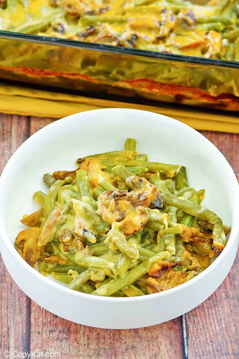 green bean casserole with cheese in a bowl in front of it in a baking dish.
