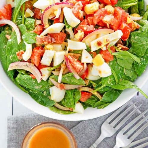 overhead view of spinach salad and a bowl of hot bacon dressing.