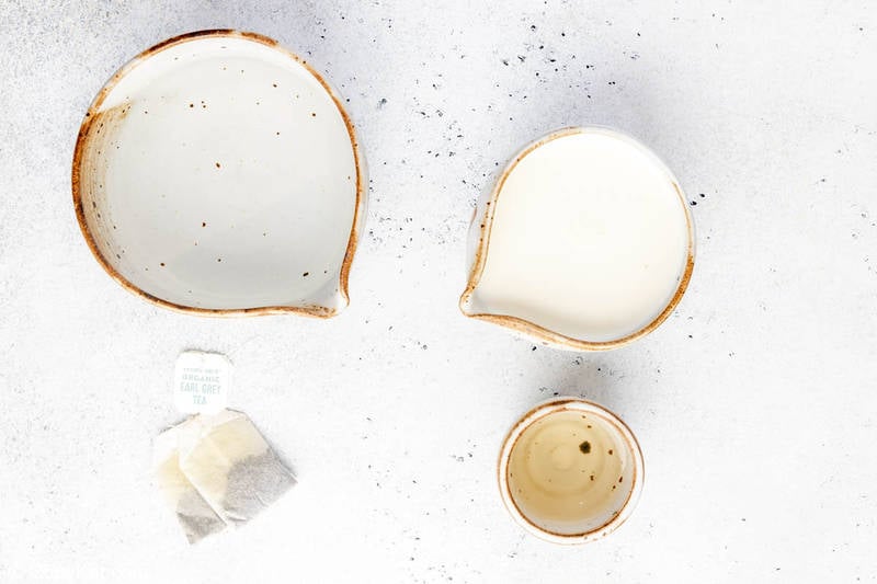 An overhead shot of the simple ingredients for a Starbucks London Fog. Pictured are two Earl Grey tea bags, and rustic ceramic pitchers containing water and milk, along with a small cup for vanilla syrup.