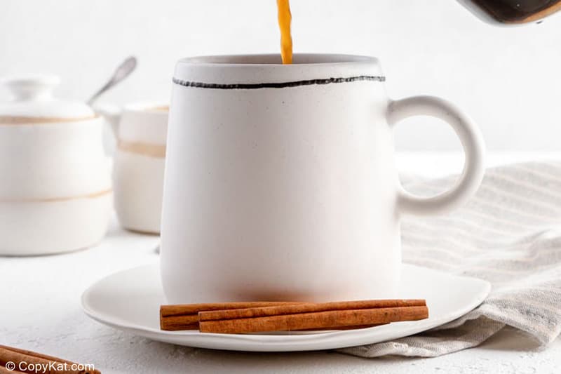 cinnamon coffee in a mug and two cinnamon sticks beside it.