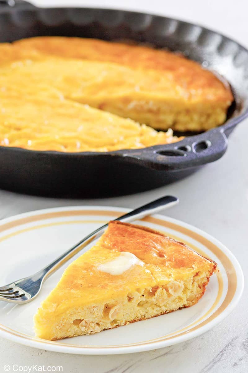 sour cream cornbread slice on a plate in front of cornbread in a skillet.