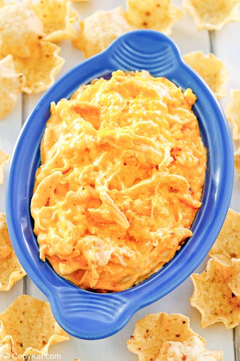 A top-down, flat-lay view of a blue oval dish filled with Frank's buffalo chicken dip. The vibrant orange, cheesy dip is centered and completely surrounded by a fan of scoop-style tortilla chips.