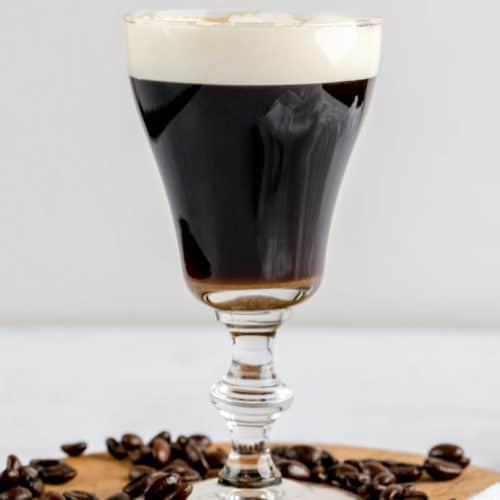 Irish coffee on a wood board with coffee beans around it.