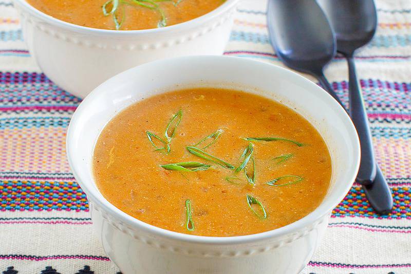 Two white bowls of creamy chicken enchilada soup, garnished with sliced green onions. The bowls are served on a colorful placemat, ready to be enjoyed.