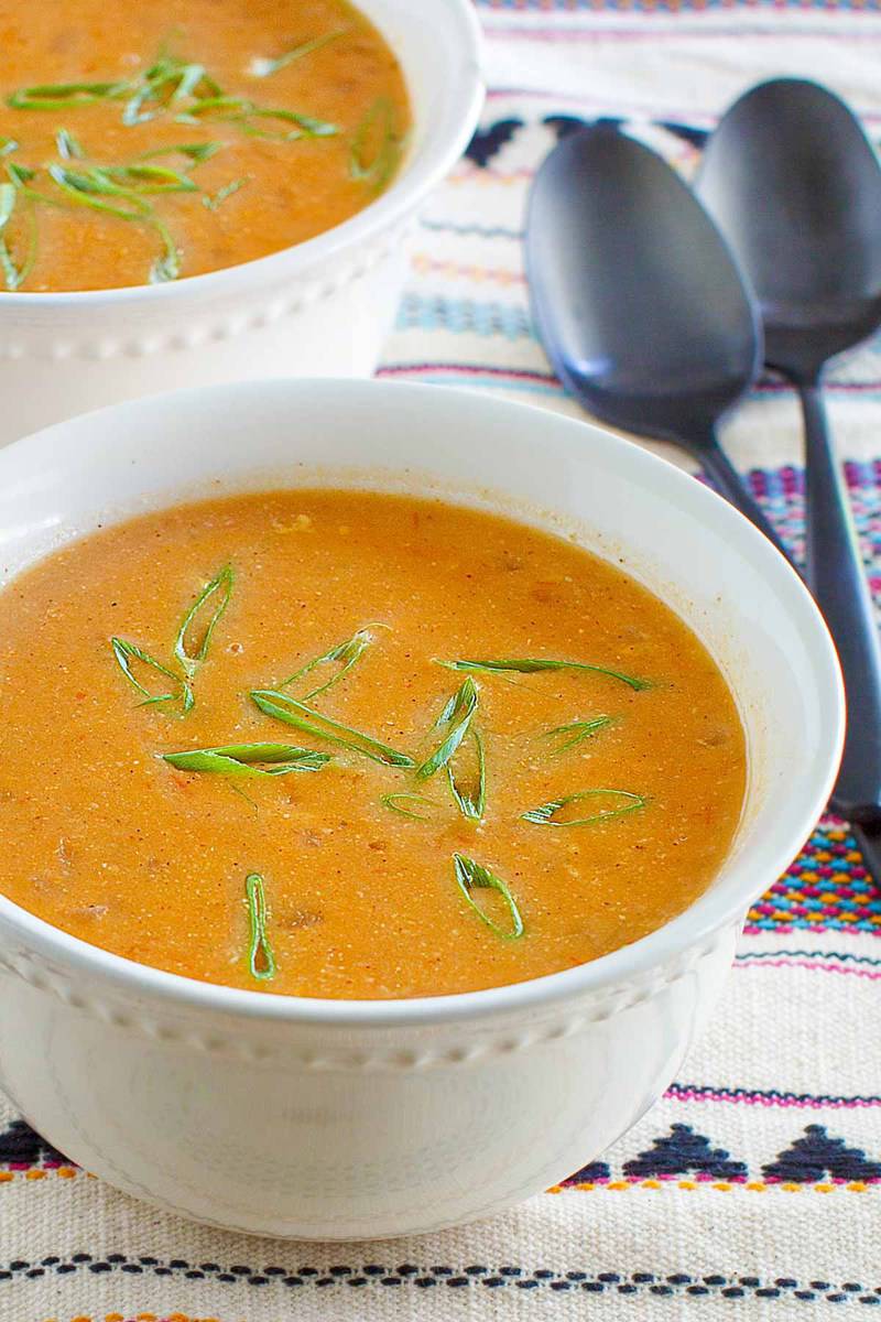 A close-up of a white bowl of creamy Chili's chicken enchilada soup, garnished with fresh green onions. The smooth, rich texture of the soup is highlighted, with another bowl visible in the background.