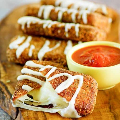 homemade Olive Garden fried mozzarella sticks and a cup of marinara sauce on a wood board.