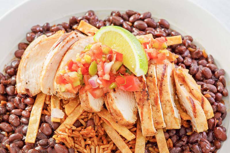 A plated serving of Chili's margarita grilled chicken. The sliced, grilled chicken is arranged over a bed of rice and black beans and is topped with pico de gallo, tortilla strips, and a lime wedge.