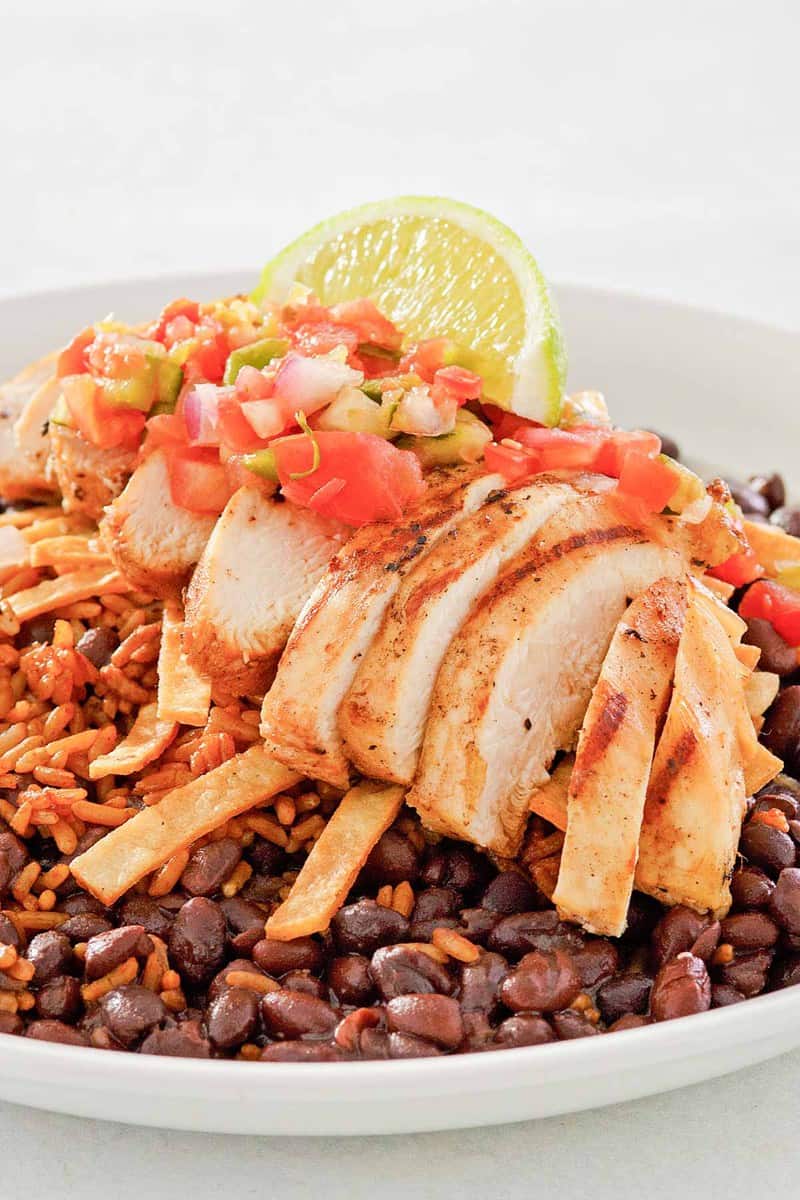 close-up of a plated margarita grilled chicken dish, highlighting the tender sliced chicken, colorful pico de gallo, and a fresh lime wedge garnish, all served over rice and beans.
