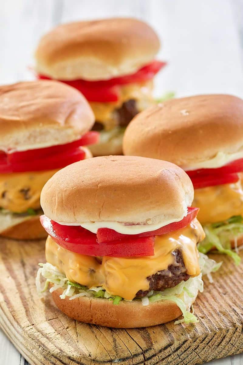 four air fryer hamburgers with cheese on a wood board.