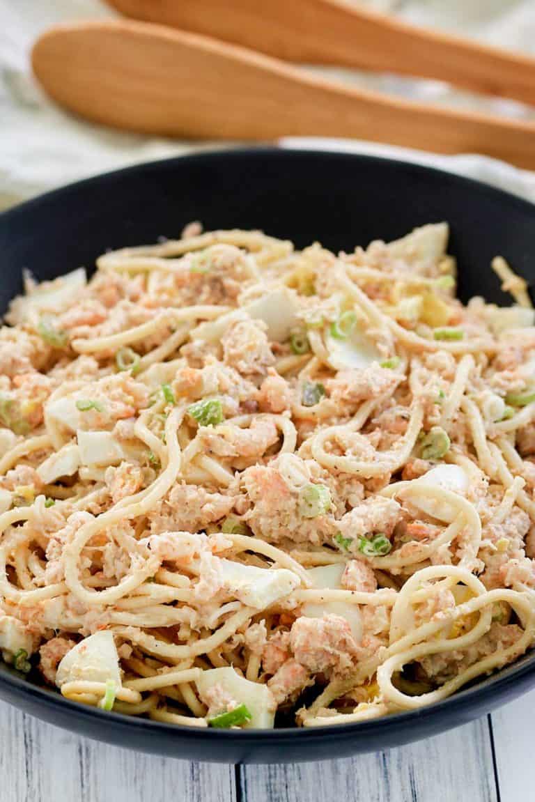 cold shrimp pasta salad in a bowl and wood salad tongs.