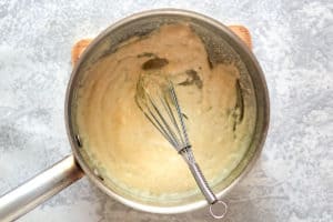 An overhead shot of a saucepan where a light blonde roux is being made by whisking flour and melted butter together to thicken the soup.